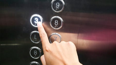 A hand pressing the number 7 button on an elevator control panel, with other numbered buttons visible.