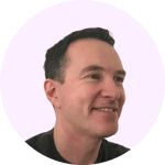 The image shows a headshot of a man with short dark hair and a friendly smile. He appears to be wearing a black shirt or top against a plain pink background.