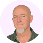 The image shows a headshot of a middle-aged bald man with a serious expression, wearing a green shirt against a light pink background.