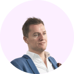 The image shows a smiling person with short dark hair wearing a blue shirt against a light pink background.