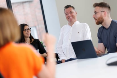 Stephen Cluskey sitting at a desk sorrounded by his colleagues 