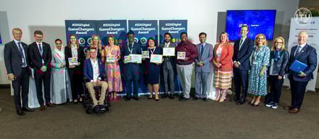 A group of people standing together, holding awards or certificates, in what appears to be a formal event or ceremony. The image shows a diverse group of individuals, including both men and women, dressed in professional attire.