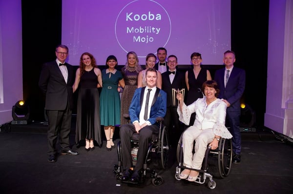 The Mobility Mojo team and partners celebrating on stage at an awards ceremony, holding the trophy