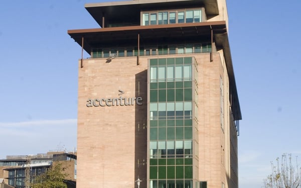 An Accenture office building in sandstone and green glass, with the Accenture sign on its side, against a blue sky