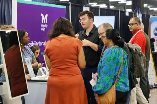 A busy Mobility Mojo stand at a conference, with a team member talking visitors through the platform