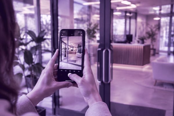 Someone from a facilities team photographing a glass entrance with their phone during an assessment