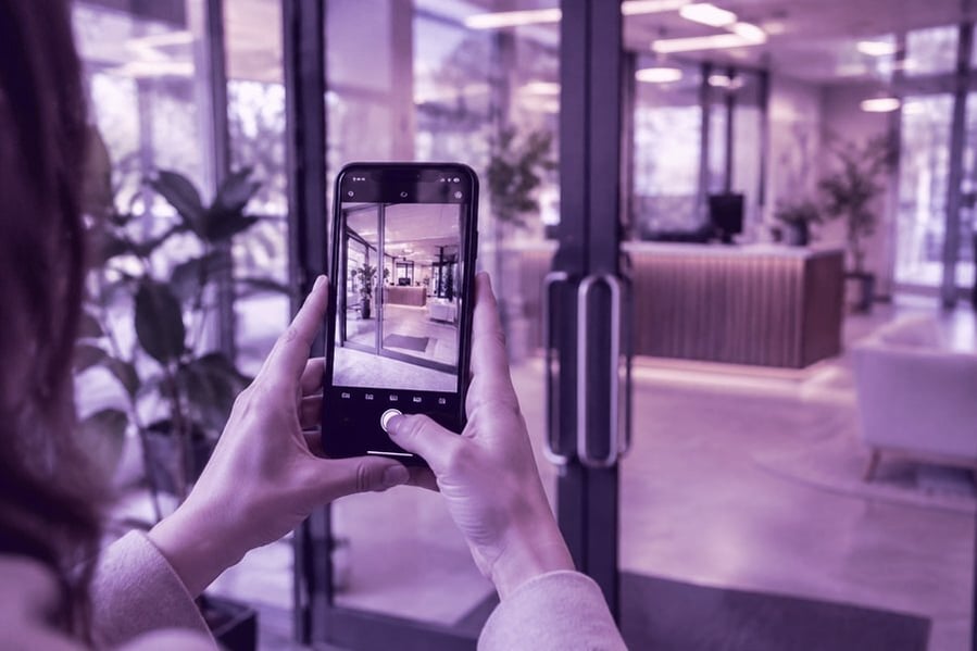 Someone from a facilities team photographing a glass entrance with their phone during an assessment