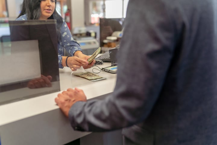A customer interacting with a bank teller. the bank teller is counting money.