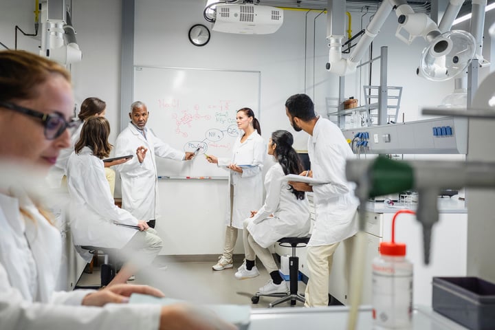 A group of people in white lab coats and scrubs working together in a medical or scientific laboratory setting.