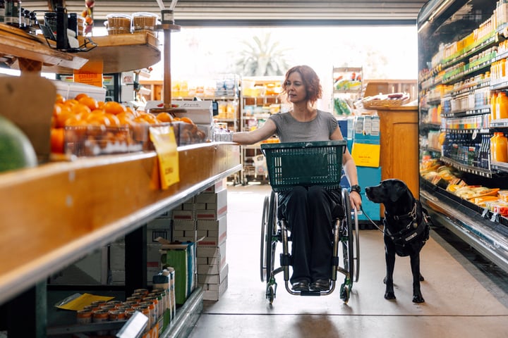 A woman in a wheelchair shopping in a grocery store, browsing the shelves and selecting items.