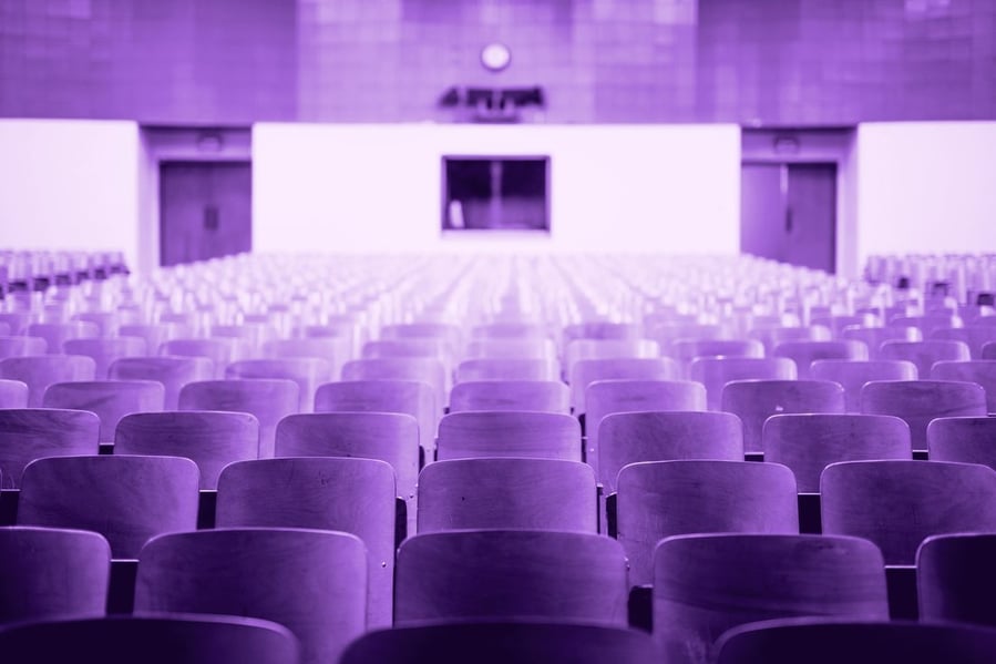 Rows of empty wooden lecture hall seats facing the front of the auditorium