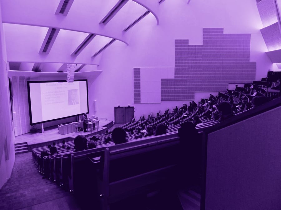 A lecture in progress in a modern university auditorium, students in tiered seating